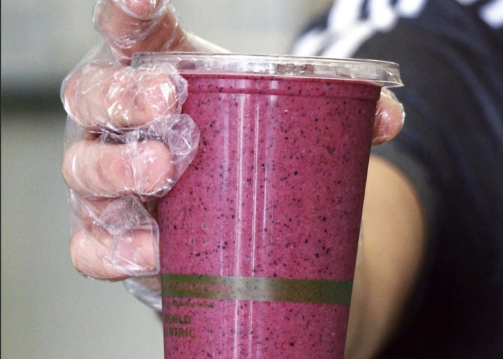 A person holds a purple takeout smoothie from Pure Juice Cafe