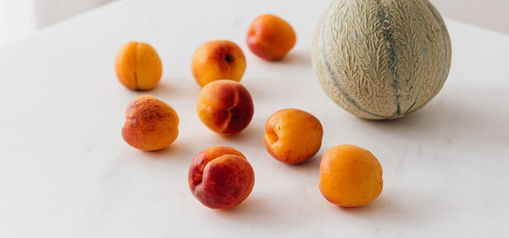Several peaches and a cantaloupe on a white surface