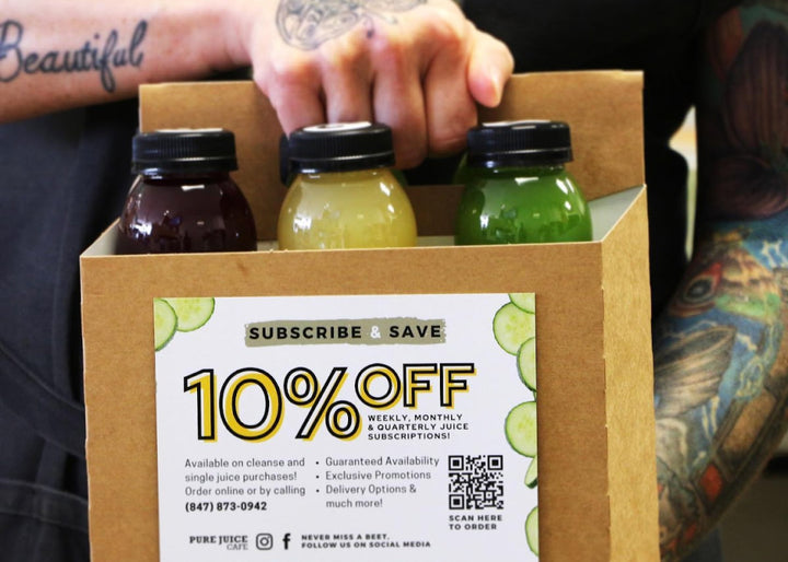 A person holds a 6-pack of Pure Juice Cafe cold-pressed juices