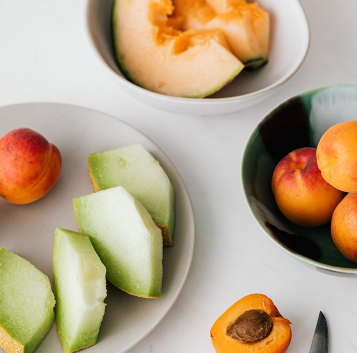 Peaches, cantaloupe and melon on dishes o a white surface