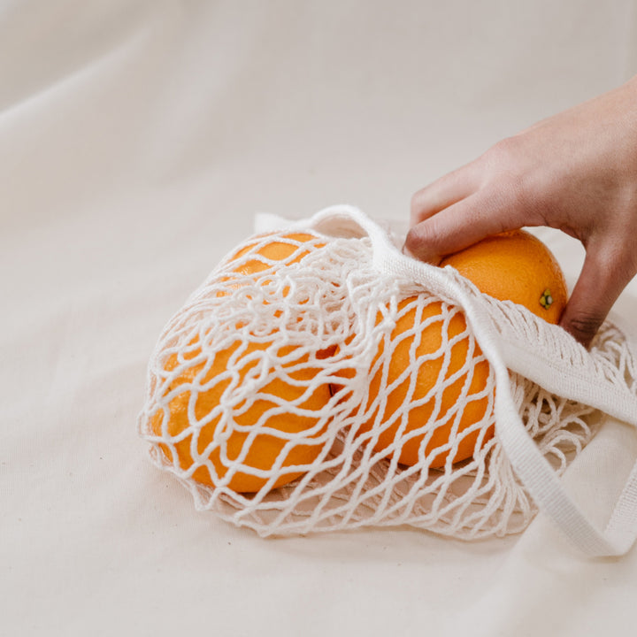 A person pulls oranges from a white net shopping bag