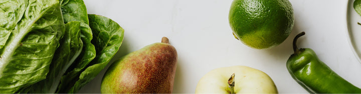 Pears, leafy greens, a lime and a chilli on a white background