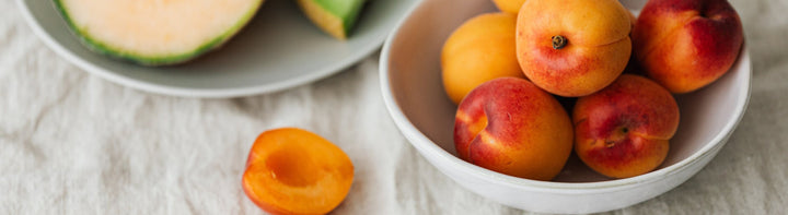 Peaches and cantaloupe in bowls on a light colored linen table cloth