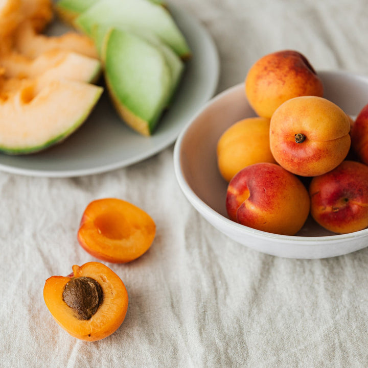 Peaches and cantaloupe in bowls on a light colored linen table cloth