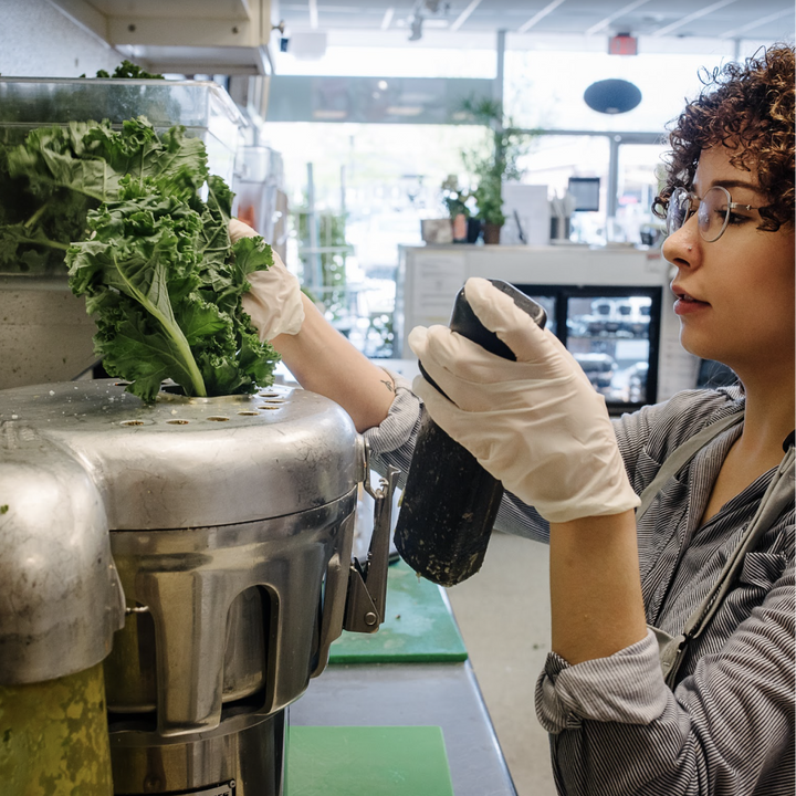 A Pure Juice Cafe employee juices a bunch of kale
